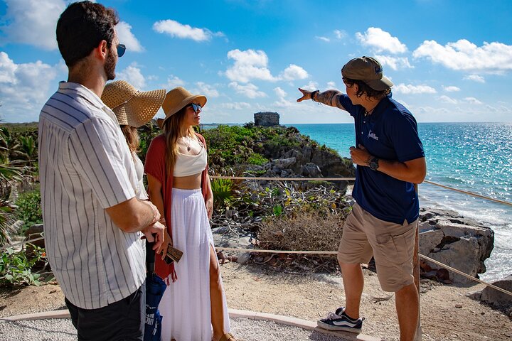 Group of friends learning alongside a tour guide about the majesty of the Tulum ruins on the iconic white coast of the Riviera Maya in the Mexican Caribbean.